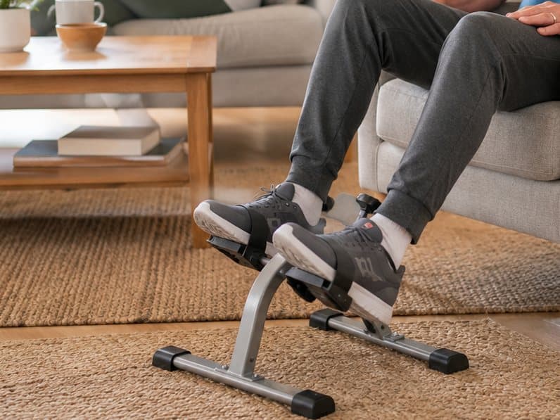 An under-desk pedal exerciser being pedalled by someone sitting back in an armchair